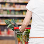 Closeup cropped view from behind of a woman shopping in a supermarket pushing a trolley full of fresh produce